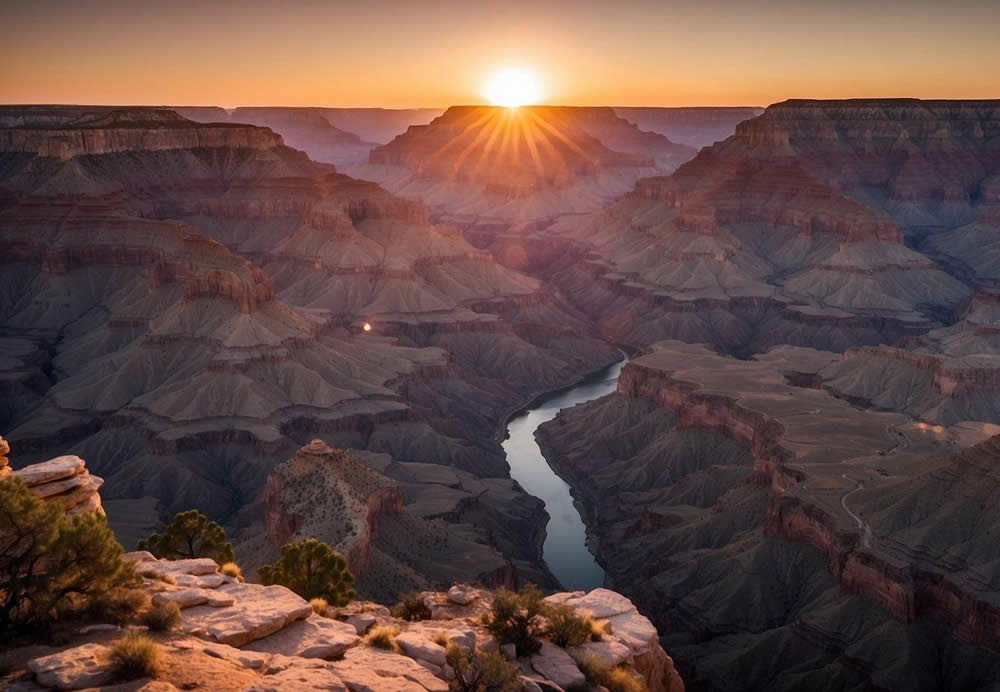 The sun sets over the vast Grand Canyon, casting a warm glow on the rugged cliffs and winding Colorado River below. The sky is painted with vibrant hues of orange, pink, and purple, creating a breathtaking scene